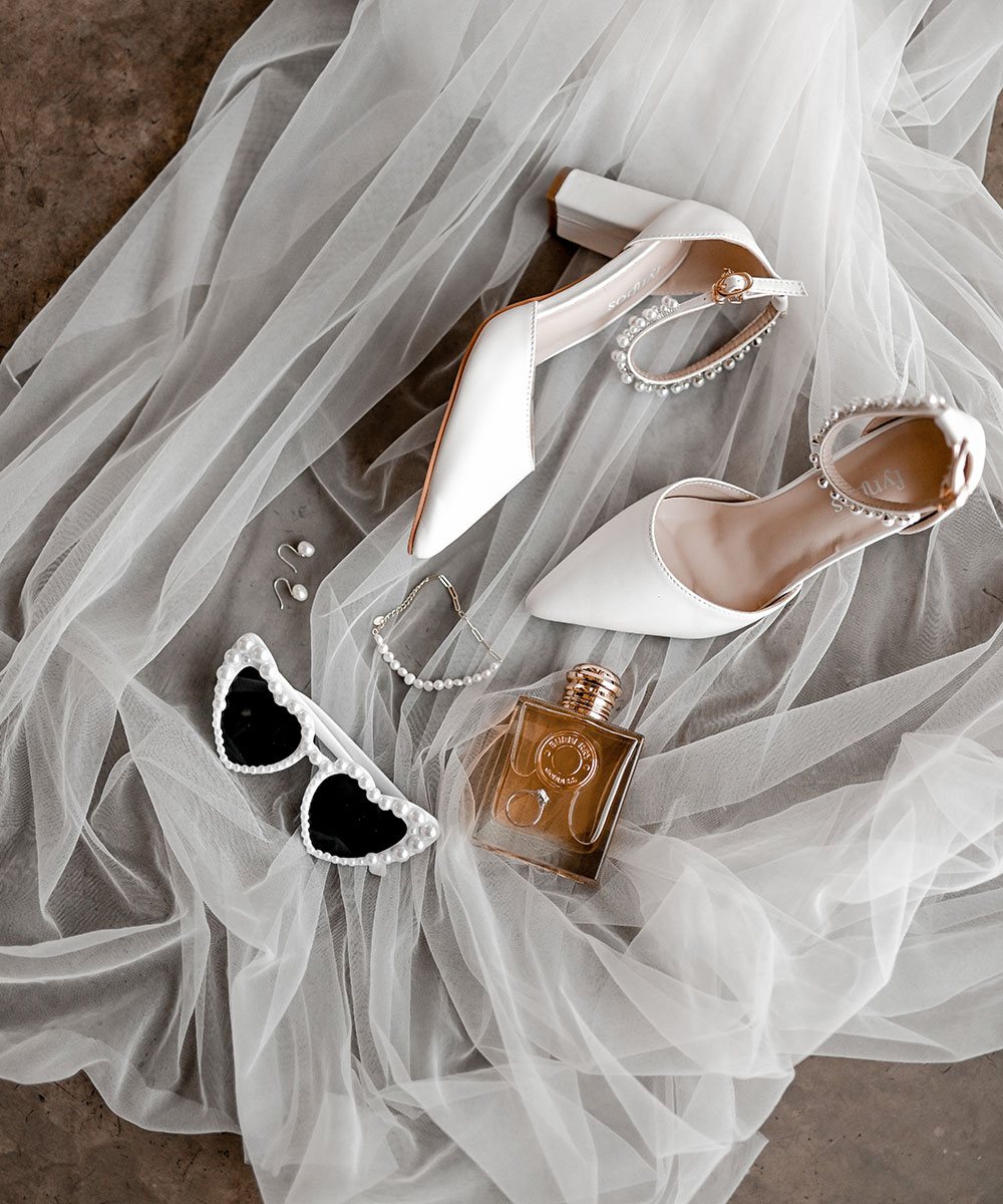 White bridal shoes, sunglasses, and perfume on a tulle background.