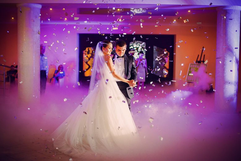 A couple dancing on their wedding day surrounded by smoke and confetti.
